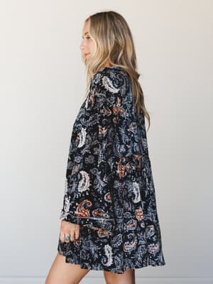 A side profile shot of a paisley-printed mini dress in deep black with cream and rust accents — the kind of dress that feels like a statement but wears like a secret.