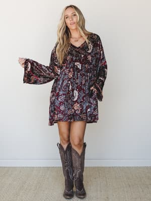 A velvet mini dress in a rich burgundy paisley print styled with tall brown cowboy boots — the kind of outfit that works just as hard at a fall concert as it does at a weekend brunch.