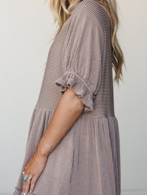 A close-up side shot of a textured striped maxi dress in warm mocha and cream, styled with turquoise and silver rings and a delicate beaded bracelet — the kind of dress that feels like a deep breath.