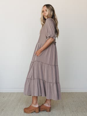 A tiered maxi dress in a warm taupe-mocha stripe worn with tan wooden clogs — the kind of dress that looks equally at home on a coffee run or a farmers market Saturday.