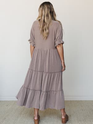 A back view of a tiered ribbed maxi dress in a warm muted mauve-brown, styled with wood-heeled sandals — the kind of dress that does a lot of heavy lifting without trying too hard.