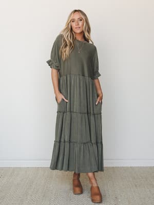 A tiered maxi dress in dark olive ribbed fabric styled with tan wood-heel clogs — the kind of effortless, lived-in look that works just as hard at a farmers market as it does at a fall brunch.