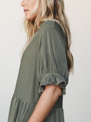 A close-up side shot of a striped dark olive maxi dress with voluminous puff sleeves and a gathered elastic cuff — the kind of dress that feels intentional and easy all at once.