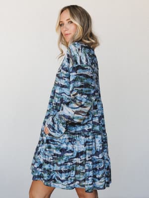 A tiered mini dress in a blue-toned camo print with long smocked sleeves — the kind of piece that reads 'I got dressed on purpose' without trying too hard.