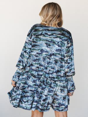 Shot from the back, a flowy blue-toned camo velvet mini dress with tiered skirt and smocked cuffs — the kind of print that somehow reads more boho than utilitarian.