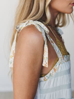 A close-up shoulder shot of a mixed-print dress with floral tie straps and lace trim detailing, layered over a mustard underlayer — the kind of dress that looks like it was made from your favorite vintage fabrics.