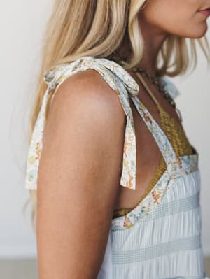 A close-up shoulder shot of a mixed-print dress with floral tie straps and lace trim detailing, layered over a mustard underlayer — the kind of dress that looks like it was made from your favorite vintage fabrics.