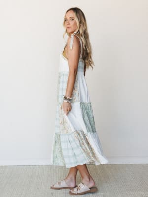 A tiered patchwork midi dress in soft ivory and sage mixes floral and plaid panels for that perfectly collected, nothing-too-precious energy — styled with stacked bracelets and footbed sandals like she's got somewhere easy and lovely to be.