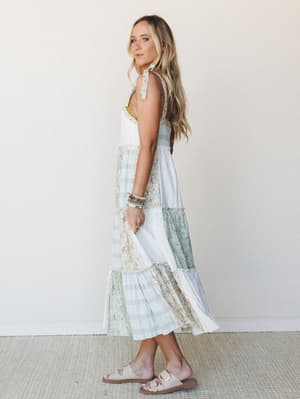 A tiered patchwork midi dress in soft ivory and sage mixes floral and plaid panels for that perfectly collected, nothing-too-precious energy — styled with stacked bracelets and footbed sandals like she's got somewhere easy and lovely to be.