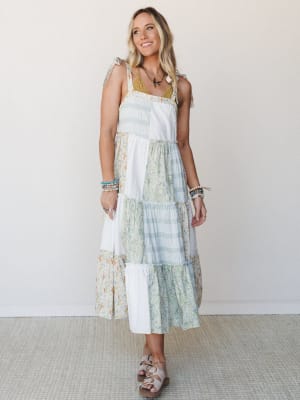 A patchwork midi dress in soft ivory, sage, and floral prints styled with layered bracelets and a bird pendant necklace — the kind of dress that makes a Tuesday feel like a road trip.