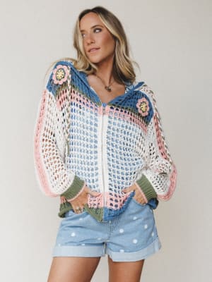 A multicolor crochet zip-up hoodie layered over a blue cami, paired with polka dot denim shorts — the kind of outfit that looks like it was thrown on effortlessly but somehow tells a whole story.