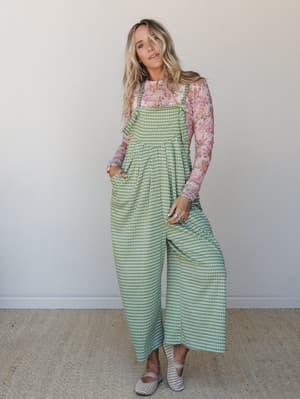 A wide-leg gingham jumpsuit layered over a long-sleeve floral top — the kind of pattern-mixing that feels effortless rather than overthought, styled with woven flats for a casual-cool finish.