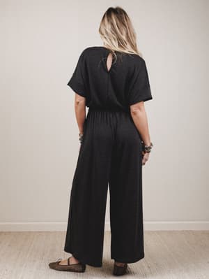 Person wearing a black jumpsuit with a plain background