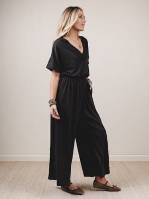 Woman wearing a black jumpsuit standing against a plain background