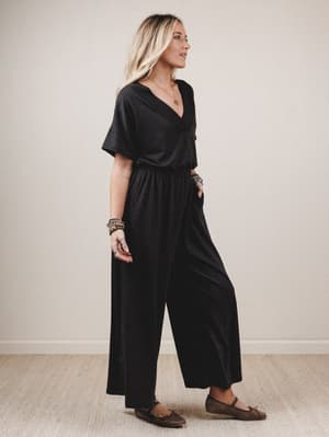 Woman wearing a black jumpsuit standing against a plain background