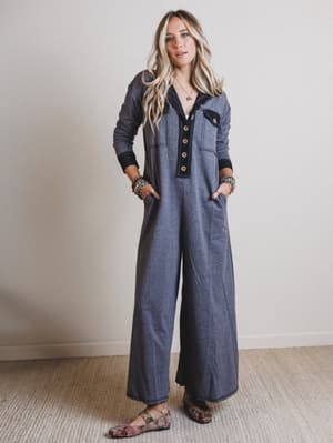 Woman wearing a long black jumpsuit with a buttoned front, standing against a plain background.
