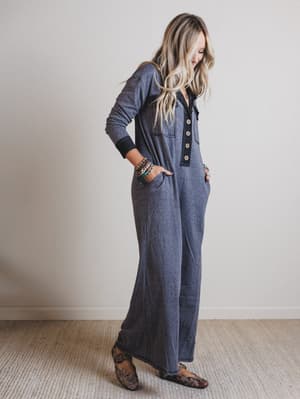 Woman wearing a black jumpsuit standing against a plain wall.