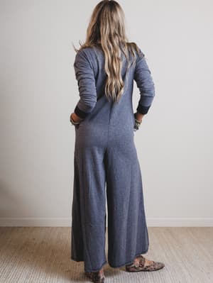 Person wearing a black jumpsuit standing against a plain wall.