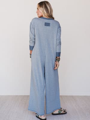 Woman wearing a long blue jumpsuit with wide-leg pants against a white background