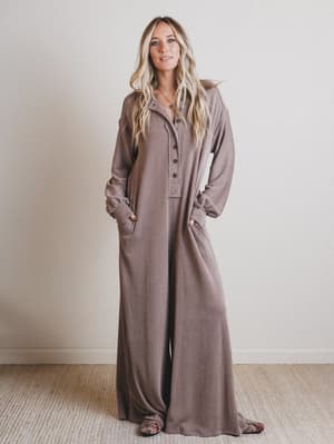 Woman wearing a long brown jumpsuit against a plain background