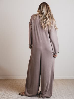 Person wearing a brown jumpsuit standing against a plain white wall.