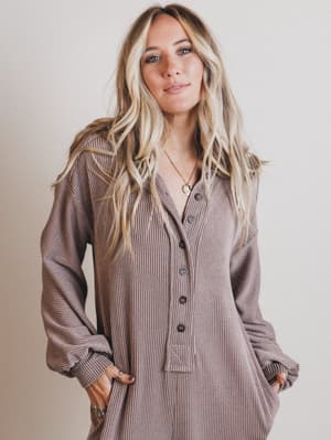 Woman wearing a long, brown ribbed dress with a button-up front against a plain background