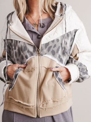 Person wearing a jacket with leopard print and beige sections on a plain background