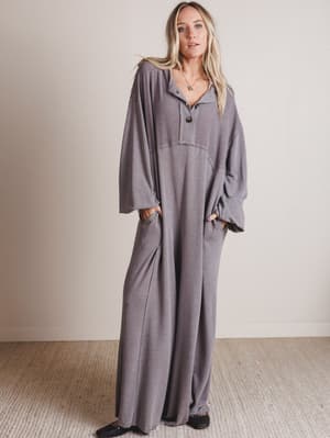 Woman wearing a gray jumpsuit standing against a plain background