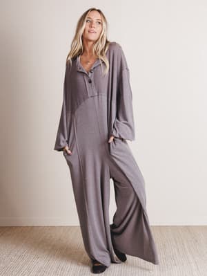 Woman wearing a long, light gray jumpsuit against a plain background