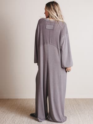 Person wearing a gray long-sleeve jumpsuit with a plain background