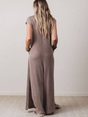 Person wearing a brown jumpsuit standing against a plain wall.