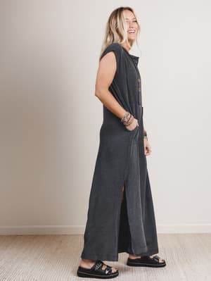 Side view of woman wearing a black and gray patterned sleeveless jumpsuit with leg slits