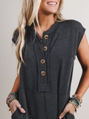 Woman wearing a dark ribbed boho jumpsuit with large buttons on a plain background