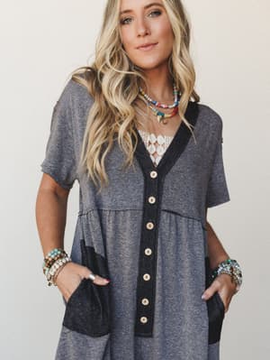 A relaxed button-front jumpsuit in heathered charcoal and black layered over a lace bralette, styled with stacked beaded necklaces and bracelet stacks — the kind of effortless outfit that looks like you tried just enough.