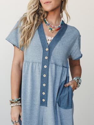 A relaxed button-front jumpsuit in soft blue-teal with contrast trim and patch pockets, styled with layered beaded necklaces and stacked boho bracelets for that effortlessly collected, everyday-magic kind of feel.