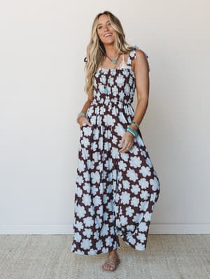 A smocked wide-leg jumpsuit in a bold brown and powder blue retro floral print, styled with turquoise jewelry and flat sandals — the kind of outfit that looks effortless but definitely got a second look.