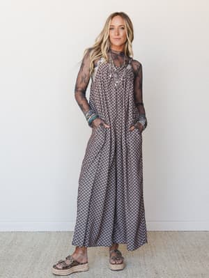 A flowy printed jumpsuit layered over a sheer black lace long-sleeve top, styled with stacked bracelets, a silver statement necklace, and espadrille platform sandals — the kind of put-together boho look that feels effortless but clearly wasn't accide