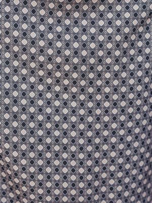 A close-up fabric shot showing a repeating geometric diamond print in cream and charcoal on a soft, drapey ground — the kind of pattern that reads as effortlessly collected without trying too hard.