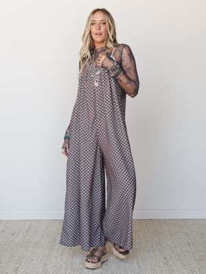 A wide-leg printed jumpsuit layered over a sheer lace long-sleeve top, styled with stacked boho jewelry and platform sandals — the kind of outfit that looks effortless but is doing a lot of intentional work.