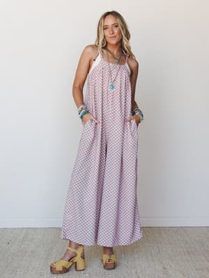 A wide-leg printed jumpsuit in soft blush and burgundy worn with yellow platform clogs, layered turquoise jewelry, and hands tucked in pockets — effortless in the best way.
