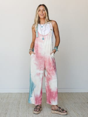 A wide-leg tie-dye overall in cotton-candy pinks and soft teal, layered over a white lace bralette and finished with turquoise jewelry and platform sandals — the kind of outfit that looks effortless but is definitely a whole vibe.