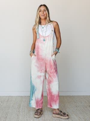 A wide-leg tie-dye overall in cotton-candy pinks and soft teal, layered over a white lace bralette and finished with turquoise jewelry and platform sandals — the kind of outfit that looks effortless but is definitely a whole vibe.