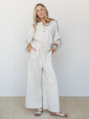 A relaxed, head-to-toe beige jumpsuit with wide-leg pants and a pullover top half styled with turquoise bracelets and flat sandals — the kind of outfit that looks effortless but clearly wasn't an accident.