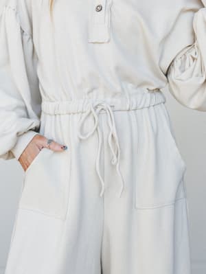A close-up mid-shot of a cream jumpsuit with a drawstring waist and patch pockets — the kind of effortless, all-in-one piece that makes getting dressed feel like the easiest decision you've made all week.