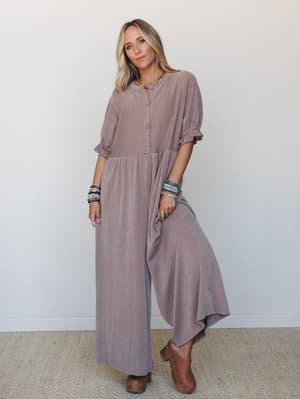 A relaxed wide-leg jumpsuit in a warm mauve-taupe ribbed knit, styled with wood-heel clogs and stacked beaded bracelets — the kind of outfit that looks effortless but is clearly very much on purpose.
