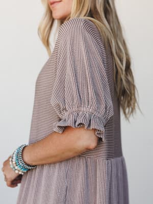 A close-up side shot showcasing the textured striped sleeve detail of a dusty mauve dress or top, styled with a stack of turquoise and pearl beaded bracelets — easy, lived-in, and quietly pretty.