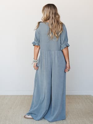 Shot from the back, this wide-leg jumpsuit in a soft seafoam stripe has an effortlessly relaxed silhouette — ruffle-cuffed sleeves, a dropped waist, and sweeping wide-leg pants that pool gently at the floor, styled with stacked beaded bracelets and t