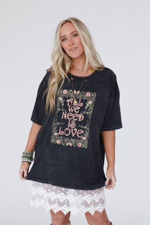 A woman with long blonde hair wears the Share The Love Graphic Tee in charcoal, styled with a white lace skirt—a chic boho look—while standing against a plain white background.