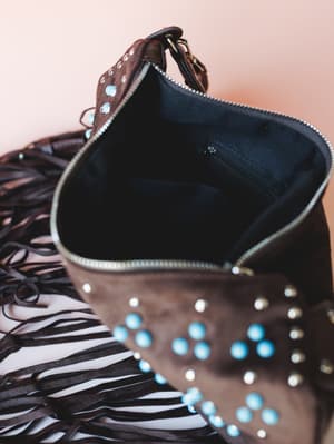 An open chocolate suede hobo bag with turquoise and silver stud embellishments and cascading leather fringe — shot close-up to show off the roomy black interior lining and interior zip pocket.