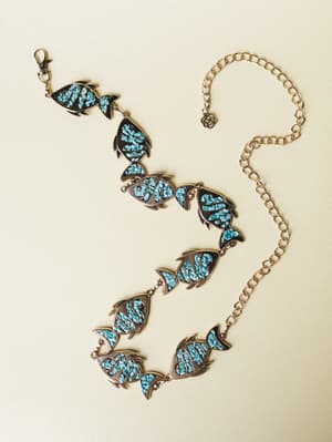 A gold chain belt laid flat, featuring linked fish-shaped charms filled with crushed turquoise stone inlay — the kind of piece that looks like it wandered in from a vintage Southwest market and never left.
